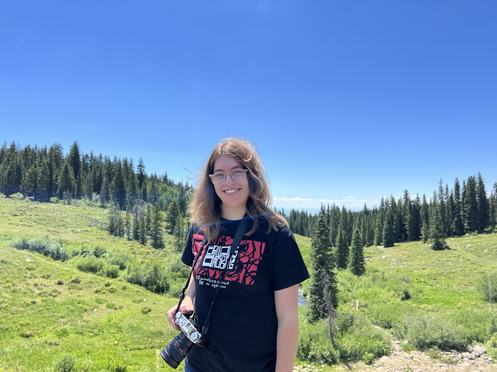 Brenna standing with a camera in the summer on the Grand Mesa.