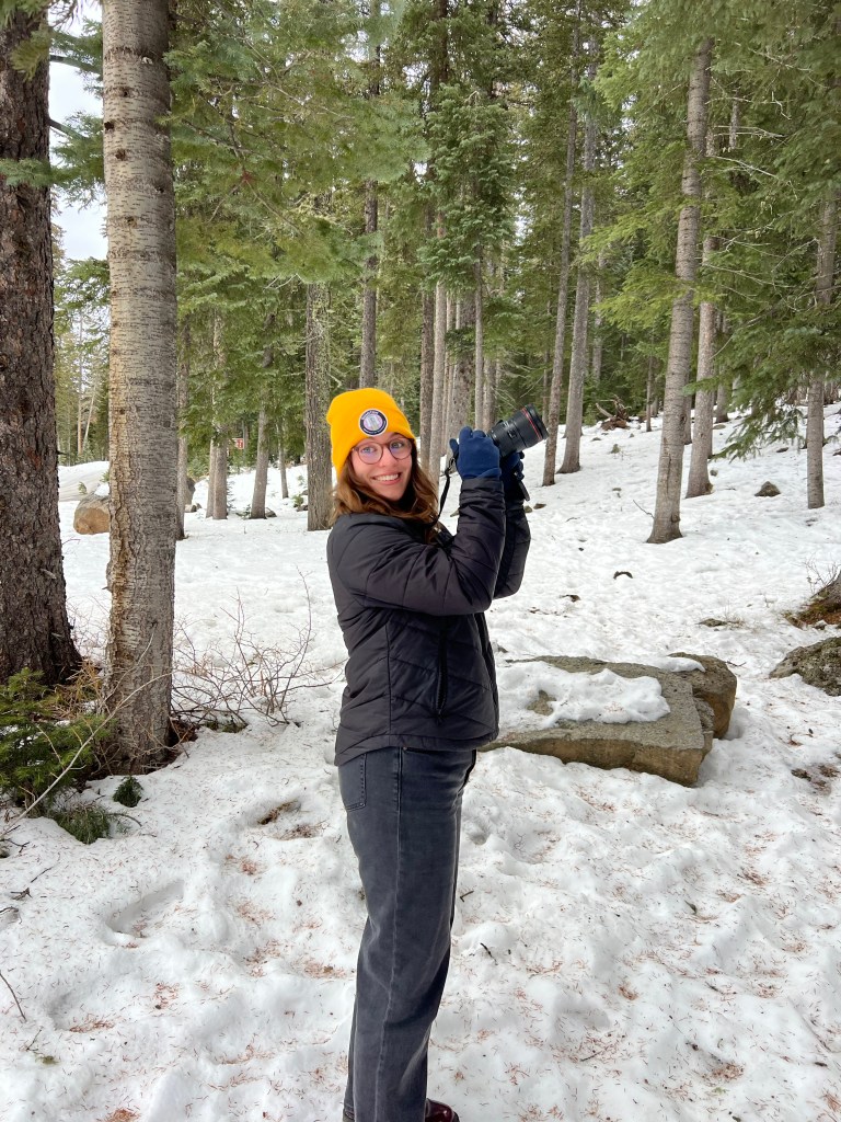 Brenna holding up a camera in a snowy landscape.
